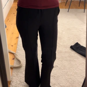 Svarta kostymbyxor - Snygga svarta kostymbyxor med medel/hög midja och bootcut-stil. Byxorna har en diskret dragkedja och knapp framtill för en stilren look. Perfekta för en elegant och sofistikerad stil.