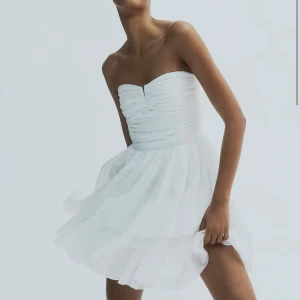 Bandeauklänning - Säljer en söt vit axelbandslös klänning med volanger.  Den är från hm och helt slutsåld på hemsidan. Den är ny med lapp kvar! 