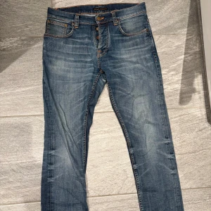 Blå jeans från Nudie Jeans - Snygga blå jeans från Nudie Jeans med orangea sömmar och klassisk passform. Säljes då de inte används längre! Perfekta för en avslappnad stil.