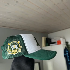 Grön och vit keps från New Era - Snygg grön och vit keps från New Era med broderad logga på framsidan. Kepsen har ett nätmaterial på baksidan för bättre ventilation och en justerbar rem för perfekt passform. Kepsen är sprillans ny så inge prutmån. 