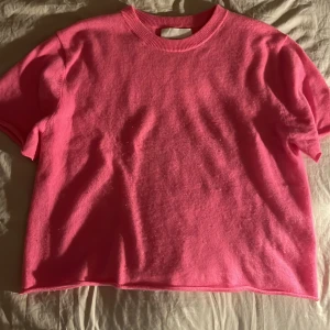 Rosa kortärmad tröja - Säljer en snygg rosa kortärmad tröja i ett mjukt kashmere material. Perfekt för en avslappnad stil. Tröjan har en rund halsringning och en enkel design som gör den lätt att matcha med olika outfits.