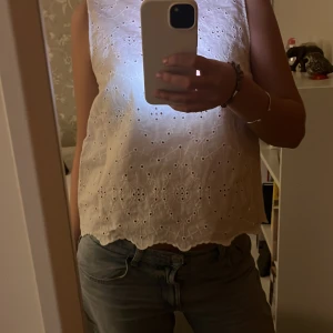 Vit ärmlös blus - Säljer en söt vit blus med broderade detaljer och vågig nederkant. Blusen är ärmlös och perfekt för varma dagar. Passar bra till både jeans och kjol.