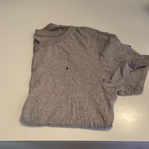 Grå t-shirt från Tommy Hilfiger - Säljer en stilren grå t-shirt från Tommy Hilfiger med en liten logotyp på bröstet. Perfekt för en avslappnad look.