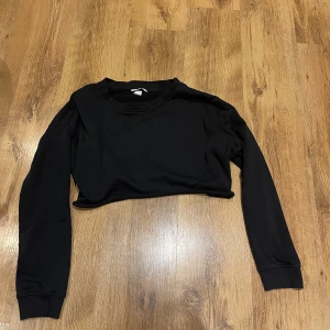 Svart croppad tröja från Basic - Säljer en stilren svart croppad tröja från Basic. Tröjan har långa ärmar och en enkel design som passar perfekt till vardags. Perfekt för dig som gillar en minimalistisk stil. 🖤