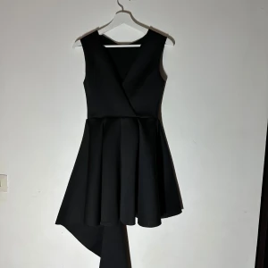 Svart ärmlös klänning - Snygg svart klänning med omlott-design och asymmetrisk nederdel. Den är ärmlös och har en elegant passform som ger en stilren look. Perfekt för en kväll ute eller en speciell tillställning.🥰🥰🥰