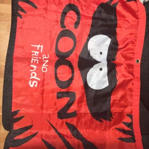 Röd flagga med Coon and Friends från South Park motiv - En röd flagga med texten 'Coon and Friends' från South Park och ett stort tryck av ögon i svart och vitt. Perfekt för fans av serien eller som dekoration.