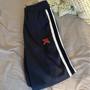 Axel Arigato Bee bird track pants - Snygga mörk blå bee bird track pants från Axel Arigato med elastisk midja och vita ränder längs sidorna. Byxorna har en broderad fågel på ena benet. Perfekta för en avslappnad stil. Knappt använda, i mycket bra skick. Storlek XS men är stora i storleken, är egentligen storlek s/m, är 175, 85kg o de sitter bra på mig!