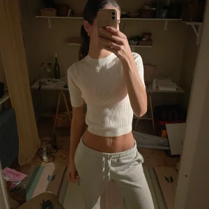 Vit ribbad topp - Säljer en stilren vit ribbad topp med korta ärmar. Perfekt för en avslappnad look. Toppen är croppad och har en rund halsringning.