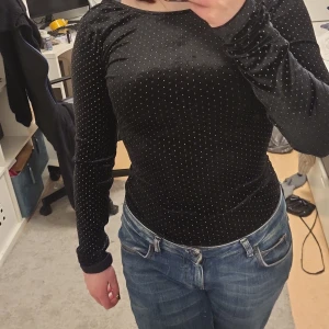 Svart velvet topp med öppen rygg - Snygg svart topp med långärmad design och en elegant öppen rygg. Perfekt för en kväll ute eller en speciell tillställning. Toppen har en tight passform som framhäver figuren. Det brukade vara ett snöre där bak. Den kan glida fram på axlarna lite