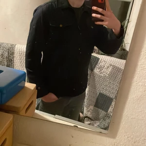 Svart Overshirt från ONLY & SONS - Säljer en stilren svart Overshirt från ONLY & SONS. Overshirten har en klassisk krage och stängs med dragkedja. Den har två bröstfickor med knappar och långa ärmar. Perfekt för en cool och avslappnad look.