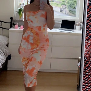 Orange/ vit klänning med öppenrygg - Storlek xs/s Färgglad sommarklänning med öppen och knytningar på ryggen. Midi/lång klänning. Använd en gång.  Kan skickas eller mötas upp i Malmö eller Göteborg!