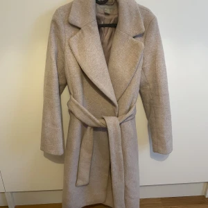 Beige kappa - Beige fodrad kappa från HM i storlek 36. På mig som är ca 160 cm lång går den ner till smalbenen. 