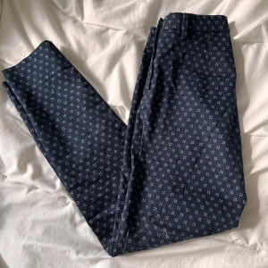 Byxor strl 32 - Mörkblå, kostymliknande byxor med vita detaljer på. Strl 32. Ankellängd. Sparsamt använda. Säljes pga för små. 