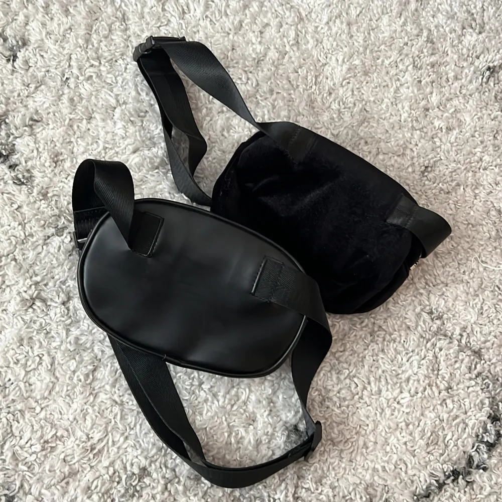 Svarta magväskor från H&M. Den ena är i imitations läder och den andra i sammet. Som nya.   19 cm breda och 12 cm höga.   Båda för 50 kr. Väskor.