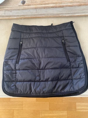 Helt ny kort täckkjol stl 36 -  Svart täckkjol från Everest med dragkedja och fickor. Kanalsydd, lätt vadderad täckkjol i kortare modell. Bra att använda över kjol, tights eller byxor för extra värme.Oanvänd. Finns i Bandhagen alt skickas. Köparen står för frakten 