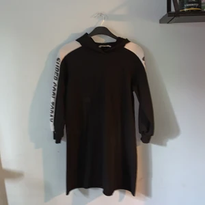 Oanvänd klänningshoodie från SHEIN  - Den är svart och har en luva. På sidan är det vitt och där står det ”Super Cool Today” bed svarta bokstäver. 