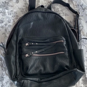 Svart väska med silver detaljer - En svart ryggsäck med silvriga detaljer. Finns totalt 8 olika fack. Använt den väldigt få gånger så den är i princip nt skick. Köpte den för 900 kr och säljer den för 200kr. 