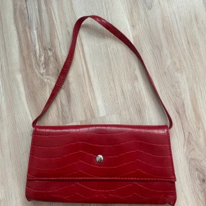 Röd axelremsväska  - Röd axelremsväska i ormskinnsimmitation!! Fint skick, superfin detalj till din outfit!! Skriv vid fler bilder elr frågor!