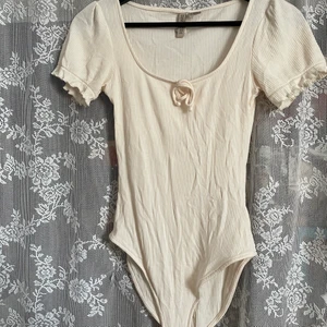 Body från H&M - Fin creme färgad body från H&M köpt begagnad men i fint skick. Tyget är strechigt. Katt finns i hemmet. Köparen står för frakten, kan även mötas upp i Uddevalla.  