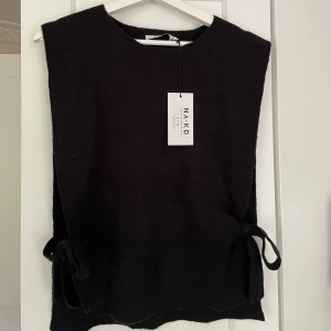 Stickad väst - En stickad väst med knytning på både sidorna. Helt oanvänd med prislapp kvar. Säljs då det ej var Min stil, passar xs/s/m!