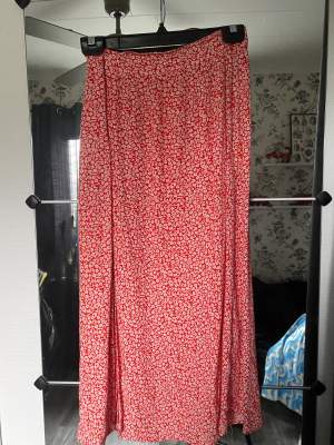 Lång röd kjol med blommor och en slits från HM. Storlek 36. 70kr plus frakt.