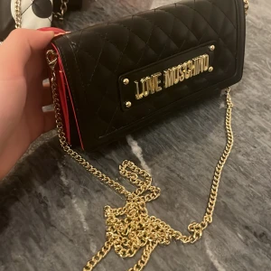 Plånboksväska Love Moschino  - Plånboksväska i svart från Love Moschino, röda detaljer inuti. oanvänd 