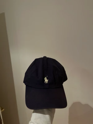 Ralph lauren keps  - Säljer marinblå ralph lauren keps pga ingen användning av den. Den har blivit använd fåtal gånger. Inga skador.