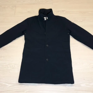 NN07 Blake - Rock / Trenchcoat, mörkblå. Fodrad med Primaloft. Varm och väldigt skön, fodrad "krage" som är avtagbar. Vindtät, vattentät med tejpade sömmar. Stretchigt tyg. Finns bra bilder på nätet. Nypris 4000 kr. I nyskick.