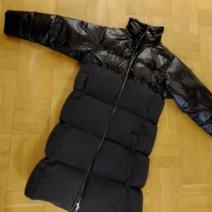 Dunkappa - Svart dunkappa i oversize stl. XS (passar stl.38) med blanka o matta partier. Superlätt och varm i nyskick!