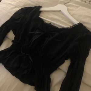 Svart långärmad blus - En långärmad svart blus med spetskanter och en liten gullig rosett. Den är cropad och funkar att klä upp och ner. Hör av er om ni är intresserade!