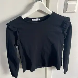 En fin svart långärmad tröja med små volanger på axlarna, har använt en gång men säljer då det inte är min stil. Köparen står för fraktkostnaden 