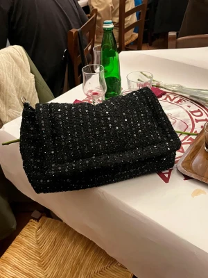 Svart glittrig väska - Säljer min helt oanvända väska från becksöndergaard med lappar kvar och allt, nypris är 1100kr. Jag säljer för 650 plus frakt!😍😍silverkedja går att justera så att man kan ha crossbody & axelväska och väskan har även ett mindre fack med dragkedja