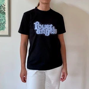 Svart T-shirt Ganni M ”Power Angels” - T-shirt från Ganni i tjock bomullskvalitet, storlek M. Använd ett fåtal gånger så skicket är perfekt. Närbilderna ger en missvisande bild av färgen då det är svårt att fotografera svart. Tröjan är ej urtvättad. 