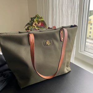 Ralph Lauren axelväska - Axelväska från Ralph Lauren i nylon. Mörkgrön färg med bruna axelband. Litet slitet skick men inga repor eller märkbara skador. 
