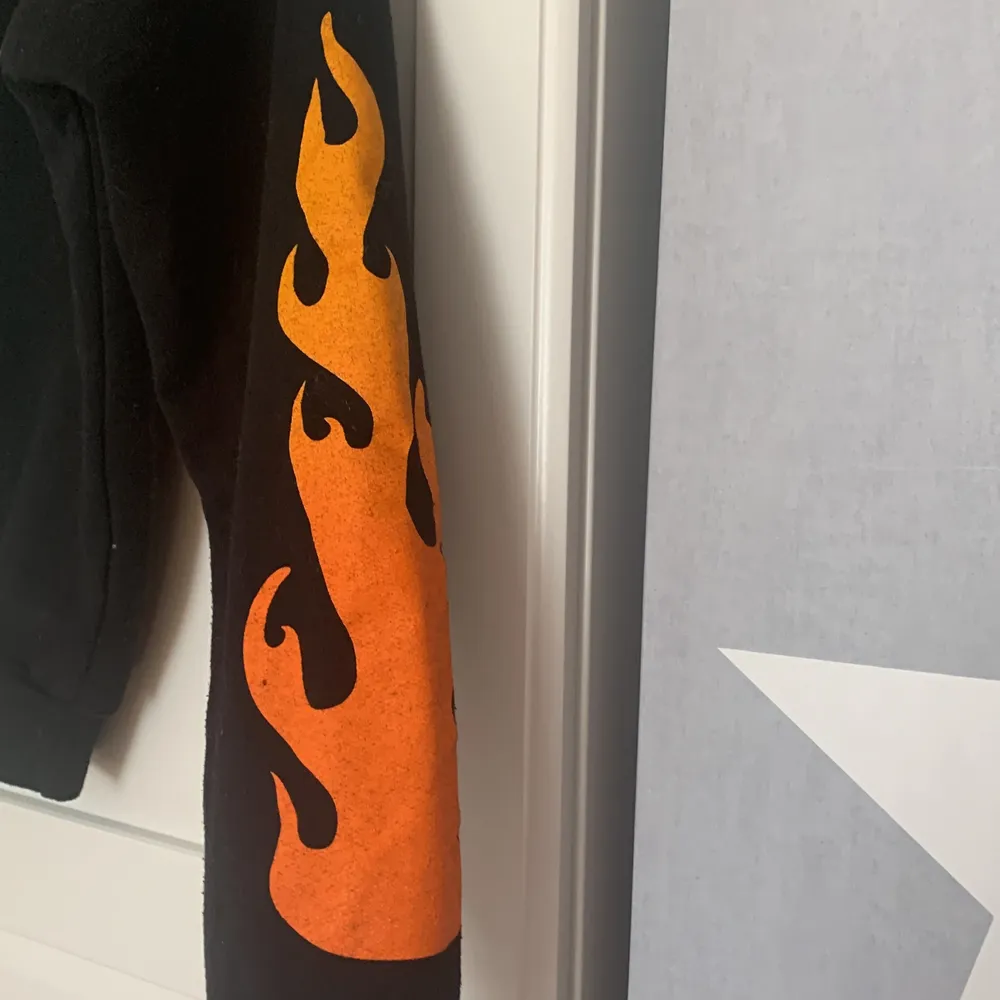 En svart munktröja med eldsflammor på armarna . Säljer den för att den inte passar längre och den är i bra skick har använt den 3 gånger och den har skönt material invändigt . Tröjor & Koftor.