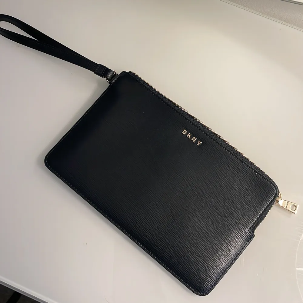 Äkta DKNY BRYANT wrislet wallet pouch i svart. Helt oanvänd, köpt för ca 9 månader sedan på Zalando, säljer på grund av ingen användning. Bevis på köpet samt fler bilder skickas vid intresse. Inget slitage. Köpt för 929 kronor. Mottagaren betalar frakt. . Väskor.