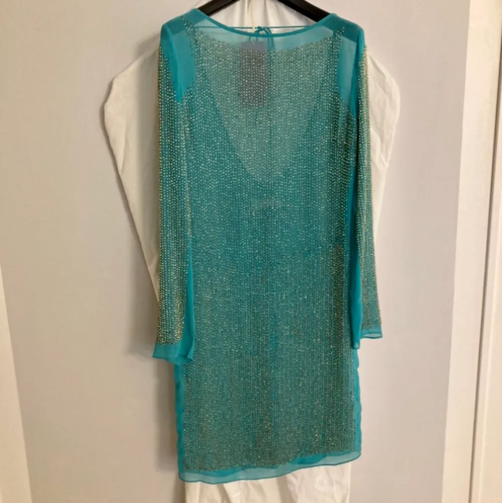 Superfin klänning från Needle & Thread som aldrig hunnit bli använd.  Är i nyskick och är handsydda pärlor i guld, samt en låg rygg med snören som man kan knyta upptill.  Skulle säga att färgen är blå,grön eller en väldigt ljus petrol. . Klänningar.