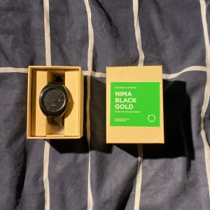 Nima Black Gold klocka CHPO - En svart klocka med gulddetaljer och armband av 100% förnybar plast. Den är för tillfället ej fungerande då jag tror batteriet är urladdat. Box tillkommer och Jämförspris är 500kr på CHPO:s hemsida och 350kr på Junkyard under rea. Pris kan diskuteras.