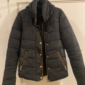 Svart jacka - Fin svart tjej/dam jacka från Vila, perfekt för hösten/vintern då den är varm och håller värmen bra men ändå är alldeles lagom varm när det börjar bli lite kyligt ute. Den sitter väldigt fint på och har en väldigt kvinnlig lock och fungerar till de mesta tillställningar och aktiviteter! Bruna och guldiga detaljer gör att jackan ser modern och lyxig ut! Använd fåtal gånger                    