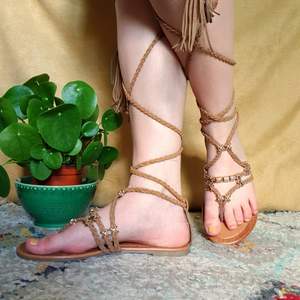 Naturbruna sandaler med detaljer i guld och långa snören som kan knytas runt benet.