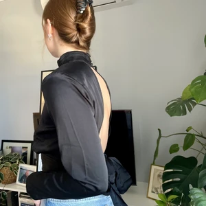 Svart satintopp - Smickrande satintopp med öppen rygg och knytning.  Endast använd vid ett tillfälle och är därför som ny. Perfekt till en middag eller fest. 