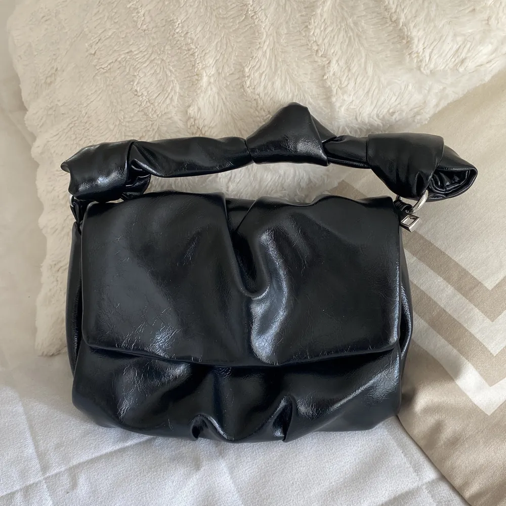 En svart mini läderväska med band som går att ta av och på . Väskor.