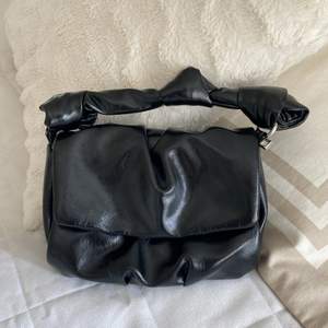 En svart mini läderväska med band som går att ta av och på 