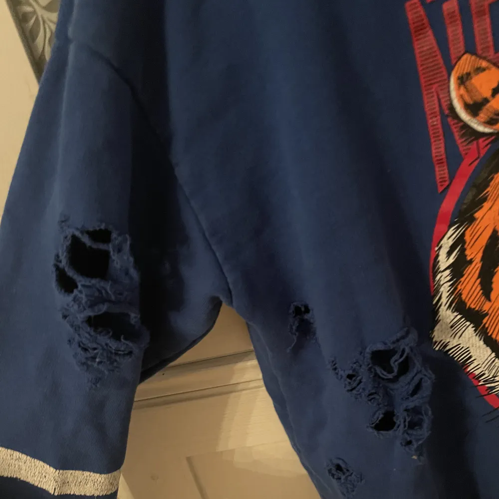 En blå sweatshirt från Ginatricot med ett tiger tryck på framsidan har tre hål som syns på bild 2&3 som fanns när jag köpte den . Tröjor & Koftor.
