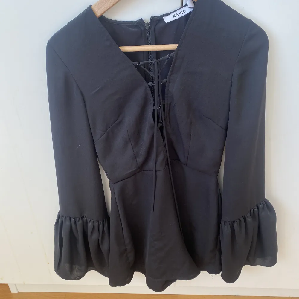 Säljer denna jumpsuit i svart från NAKD. Den har lite knytningar vid brösten och är väldigt bekväm så man kan både klä upp och klä ner den. Den är i lite silkes polyester material. Blusar.