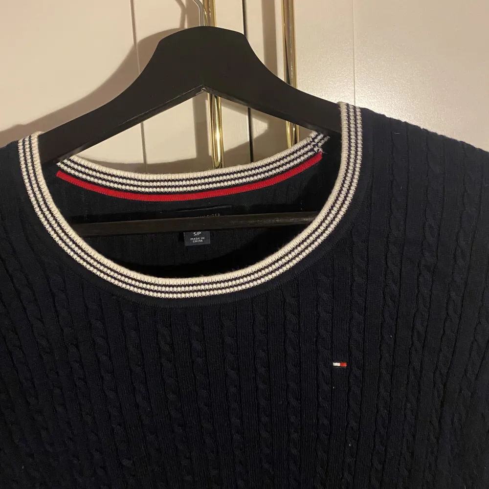 Marinblå kabelstickad tröja från Tommy Hilfiger, med vit/blå-randig detalj i krage och ärmar. Nypris 1199kr.. Stickat.