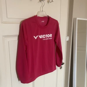 Träningströja från Victor - Säljer denna snygga träningströja från Victor. I fint skick. Storlek XS. 100% polyester. Färgen är ceriserosa. Perfekt till uppvärmingen inför träningen. 