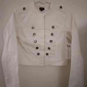 NY & OANVÄND vit snygg jeansjacka / vårjacka i soldat-stil. Strlk: 36/SMALL. - Helt NY och oanvänd vit (kritvit, inte gräddvit) army/military/soldat-jacka /vårjacka i jeanstyg med en del stretch i tyget, från Lindex. Storlek: 36/SMALL men passar eventuellt även någon med 32-34/XS. Stängs med dragkedja. FRAKT TILLKOMMER.