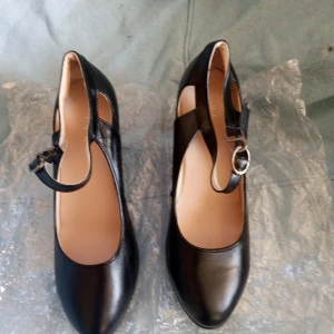 Pumos svarta med vristrem stl 38 /39. - Helt nya och oanvända svarta pumps i skinnimitation liknande material med vristrem .klackhöjd 7 cm. Ligger i sin original förpackning .hämtas i Skene alt skickas .