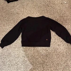 Svart tjocktröja - Svart långärmad tjocktröja som går lite off shoulder och är kort lite som en magtröja och puffärmar